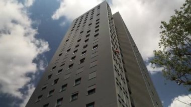 4K Zaman atlamalı tırmanışçılar mavi gökyüzünde uçan bulutlara karşı büyük ve modern iş dünyası Gökyüzü Kulesi 'nin camlarını siliyorlar