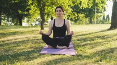 Kız Lotus pozisyonunda yoga minderinde oturuyor. Gözleri kapalı, dışarıda yoga ve meditasyon yapmaya hazırlanıyor. Vücut ve ruh sağlığı konsepti