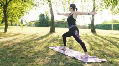 Spor salonundaki atletik kız, savaşçı pozuyla dışarıda yoga yapıyor. Vücut ve ruh sağlığı konsepti.