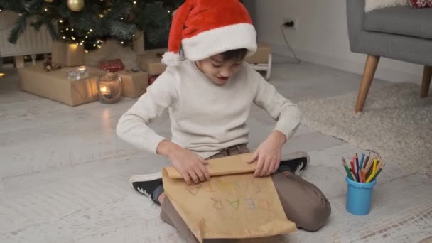 Счастливый Маленький Мальчик Новогодней Шляпе Готовит Письмо Санта Клаусу Сидя — стоковое видео