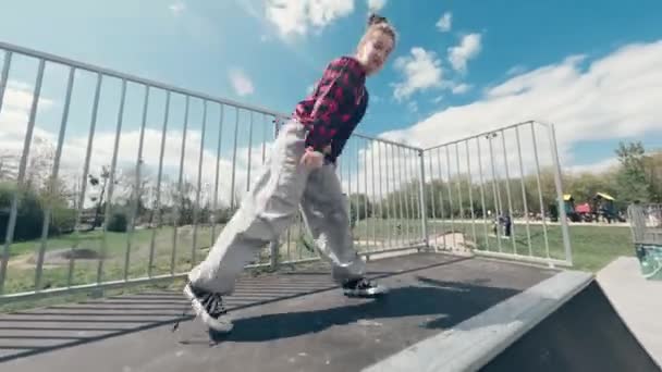 エクストリームパークのスケートランプでダンスと現代のヒップホップダンスの広いズボンの素敵な若い女の子 — ストック動画