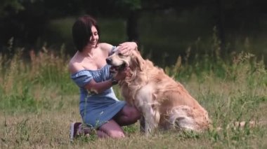 Güzel kız sahibi Golden Retriever köpeğine sarılıyor ve doğaya gülümsüyor. Yaz zamanı safkan evcil köpek labrador 'unu okşayan genç bir kadın.