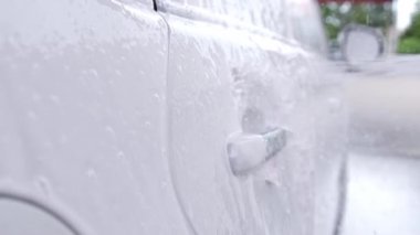 Sabunlu su jetleri yavaş çekimde oto yıkama istasyonunda bir arabayı temizler.