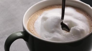 Kız eli kapuçino bardağında kaşıkla şeker karıştırıyor. Taze kahve, latte köpüklü makro manzaralı.