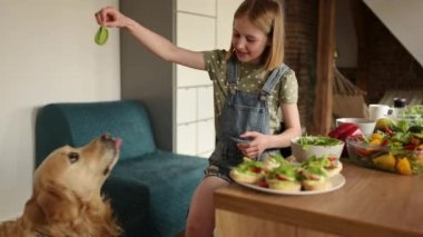 Şirin küçük kız mutfakta sağlıklı sebze kahvaltısı yapar ve altın av köpeğiyle oynar ve köpek ıspanak yapraklarını besler.