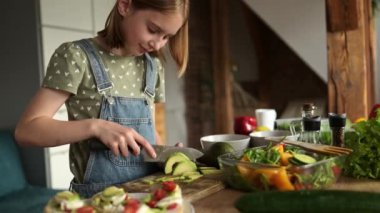 Mutfaktaki sağlıklı sebze salatası için küçük tatlı bir kız kesim ve avokado.