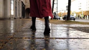 Uzun kırmızı etekli ve siyah çizmeli bir kadın yağmurdan sonra sonbahar caddesinde yürür, arkadan bakar.