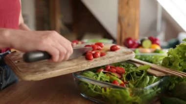 Kız mutfaktaki salataya vişneli domates ekliyor.