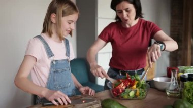 Anne güzel kızına sebze salatası pişirmeyi öğretiyor.