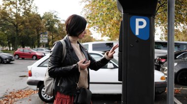 Kadın, otopark parkmetresi üzerinden kredi kartı kullanarak para ödüyor.