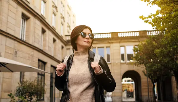 Attractive stylish Woman In Sunglasses Walks By City Street With Backpack