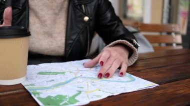 Şık bir bayan turist caddedeki kafede kahvesini yudumlarken şehir turistik güzergahını haritada kontrol ediyor.