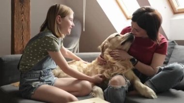 Genç bir kadın ve genç bir kız Golden Retriever köpeğini okşuyor ve evde gülümsüyor. Anne, kız ve safkan evcil köpek aile anları.