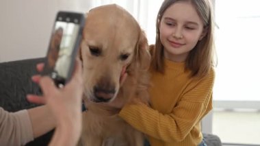 Akıllı telefonlu bir kız evde Golden Retriever köpeği ve ergen bir çocuğun fotoğrafını çekiyor. Kadın anne fotoğrafı, cep telefonu kamerasıyla safkan bir evcil köpek ve kız çocuğu fotoğrafı yaratıyor.