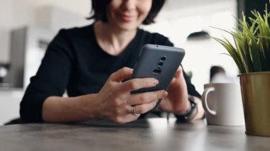 Genç bir kadın internette akıllı telefon kullanıyor ve mutfakta gülümsüyor.