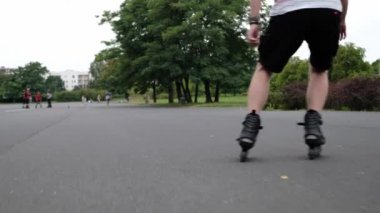 Yazın parkta paten çalışması yapan genç bir adam. Tekerlekli sandalyedeki adam arka plandaki hareketlerin keyfini çıkarıyor.