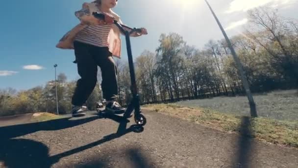 阳光明媚的日子 一个漂亮可爱的小女孩在外面的溜冰场由一个Kickstarter开车 — 图库视频影像