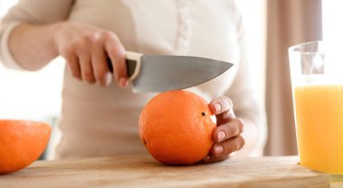 Girl cut ripe orange with knife for making natural juice at kitchen. Woman hand preparing tropical fruit drink