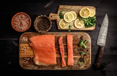 Somon balığı filetosu, otlu ve limonlu. Siyah bir masada sağlıklı bir akşam yemeği için hazır.