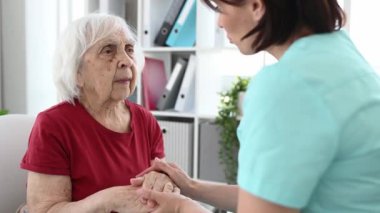Sağlık çalışanı yaşlı kadınların elini tutuyor ve onu sakinleştiriyor.