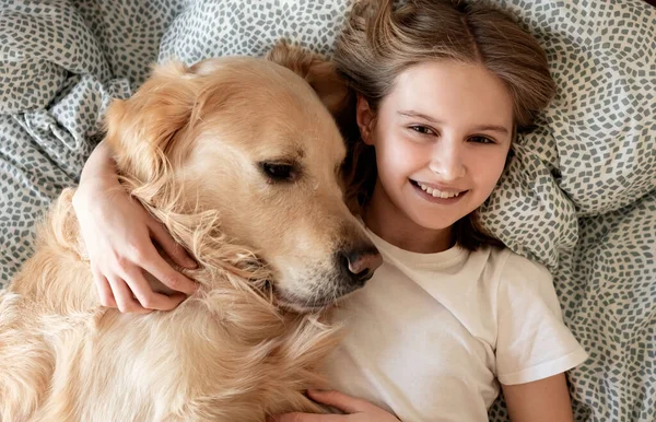 Boldog Kislány Öleli Golden Retriever Dog Mosolygó Hazugság Ágyon Jogdíjmentes Stock Fotók