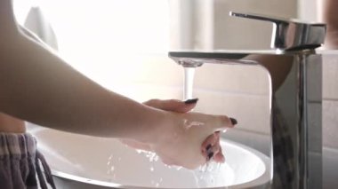 Kız ellerini lavaboda yıkıyor. Karıştırıcı musluğunu kullanıyor.