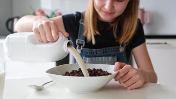 彼女の乾燥した朝食のためのブラウンチョコレートボールのプレートにミルクを注ぐ小さな少女 — ストック動画