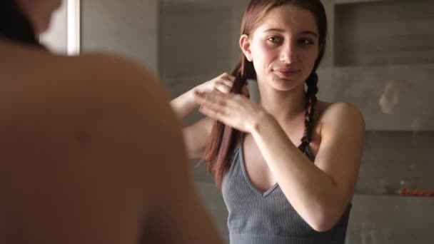 Νεαρό Κορίτσι Πλέκει Μαλλιά Της Στον Καθρέφτη Του Μπάνιου Πρωί — Αρχείο Βίντεο