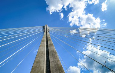 Parlak mavi gökyüzüne karşı halatlarla büyük metal köprü desteği