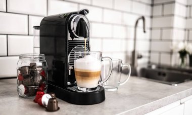 Kapsüllü kahve makinesi evdeki mutfakta şeffaf bardakta kapuçino hazırlıyor. Espresso kafein üreticisi ve kremalı İtalyan içeceği.