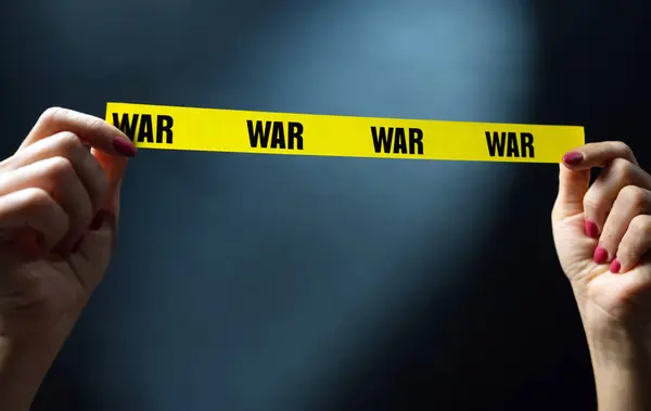 Warning Hands Holding Yellow Tape With War Text As Symbol Of Safety And Stop Conflict. Concept Of Invasion And War
