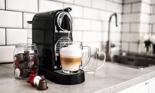Coffee machine with capsules preparing cappuccino in transparent cup at domestic kitchen at home. Espresso caffeine beverage maker and creamy italian drink