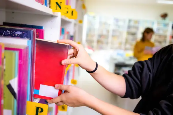 Fille Prenant Livre Rouge Des Étagères Dans Bibliothèque École Lumière Image En Vente