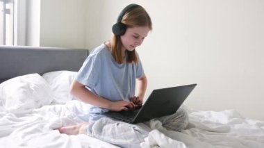 Tatlı genç kız yatak odasında büyük bir yatakta otururken interneti karıştırıyor.