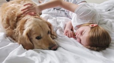 Tatlı küçük kız, sevgili evcil hayvanıyla yatakta uzanırken büyüleyici köpeğini nazikçe okşuyor.