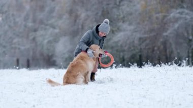 Kışın bir kar tarlasında sevimli altın av köpeğini okşayan kadın.