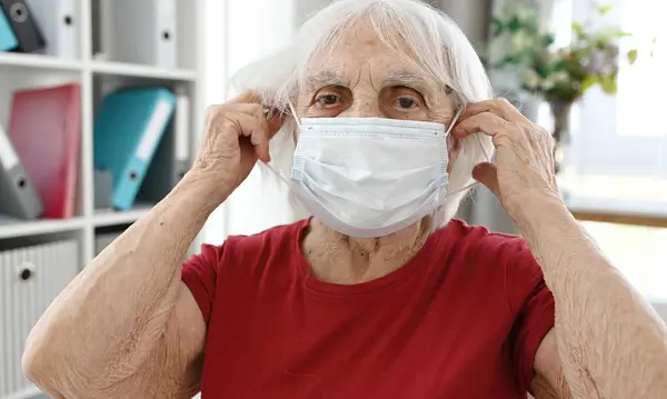 Ηλικιωμένη Γυναίκα Βάζει Στην Προστατευτική Ιατρική Μάσκα Στο Πρόσωπο Εικόνα Αρχείου