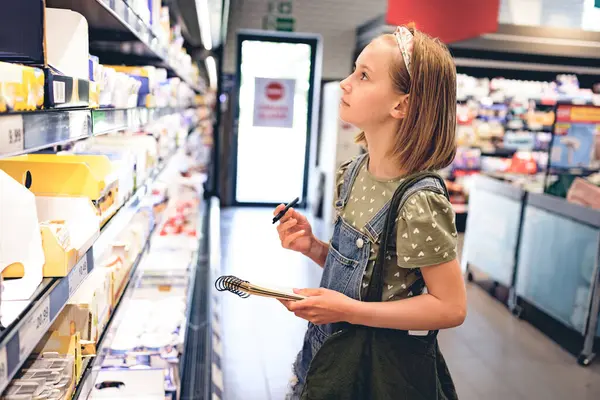 Smuk Pige Barn Købe Med Indkøbsliste Supermarkedet Ser Productson Hylde Stock-foto