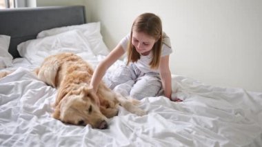 Küçük kız tatlı köpeğini nazikçe okşuyor. Yatakta yatıyor.
