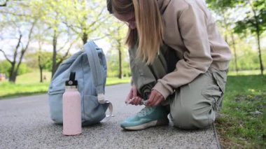 Sırt çantalı, ayakkabı bağcıklarını parkta takan küçük bir kız.