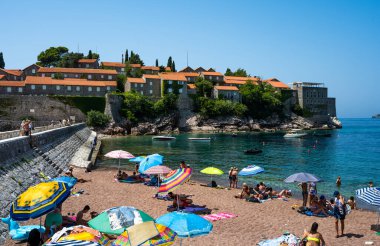 Budva, Karadağ - 27 Temmuz 2021: Güneşli bir günde Karadağ 'ın Budva kentindeki Sveti Stefan adasında sahil. Adriyatik Denizi 'ndeki lüks tatil beldesi