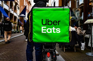 Lahey, Hollanda - 09 Nisan 2023: Büyük yeşil Uber Gıda Torbası Yiyor. Bisikletle yemek getiren adam.