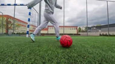Çocuk futbol oynuyor, futbol sahasında topla pratik yapıyor.