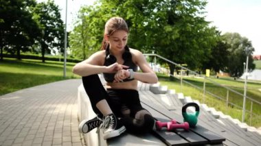 Akıllı bir spor saati kullanarak parkta egzersiz yapan zinde bir kız.