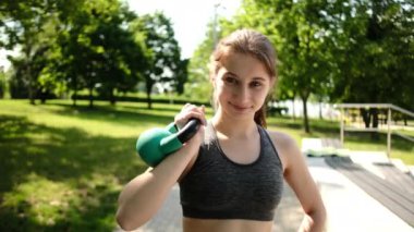 Fit kız parkta elinde bir kettlebell ile egzersiz yapıyor.