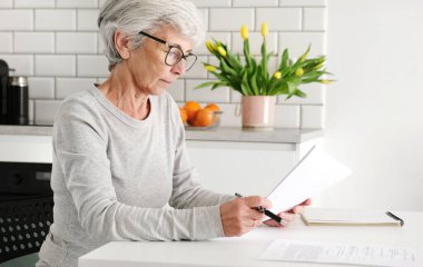 Evdeki evrak işleri ve anlaşmalarla uğraşan yaşlı bir kadın.