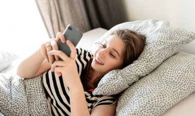 İnternette Sörf Yapan Genç Bir Kız Akıllı Telefonla Yatakta Yatıyor