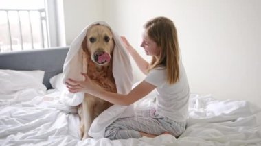 Neşeli genç kız altın av köpeğiyle eğleniyor, battaniyeye sarılı.
