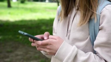 Küçük liseli kız parkta telefonuna mesaj yazıyor.