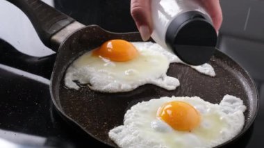 Kızarmış tavada yumurta üzerine tuz serpiştiren kadın.